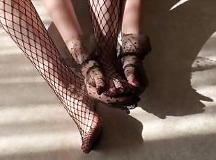 The girl caresses her legs in fishnet tights and strokes them with her hands in lace gloves